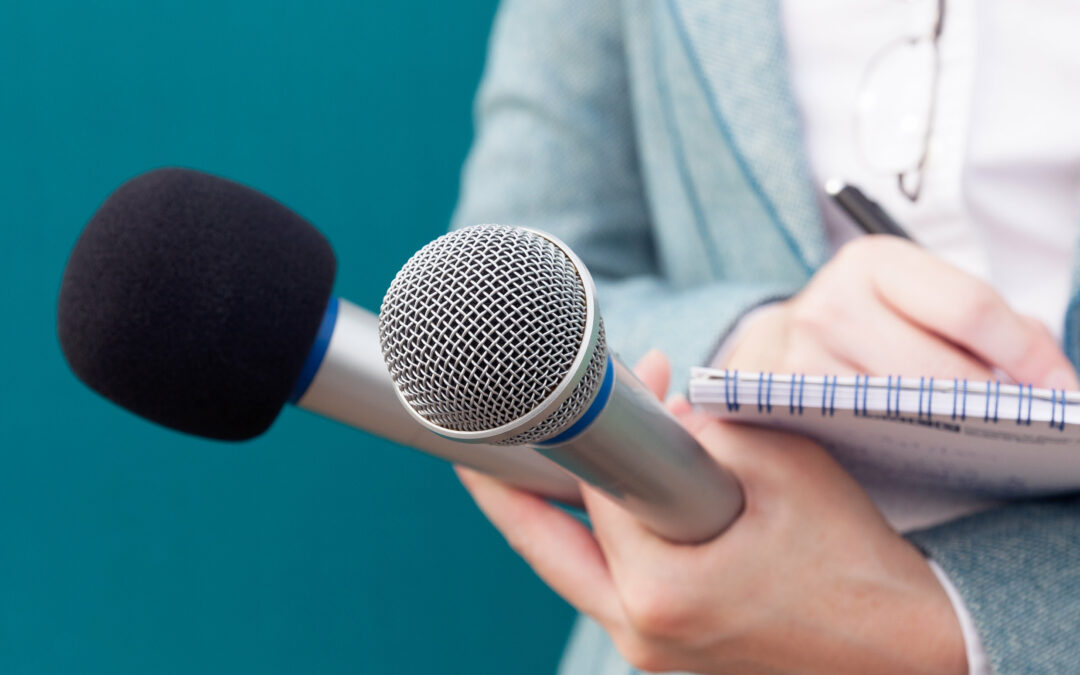 Reporterin mit Notizblock und Mikrofonen in der Hand