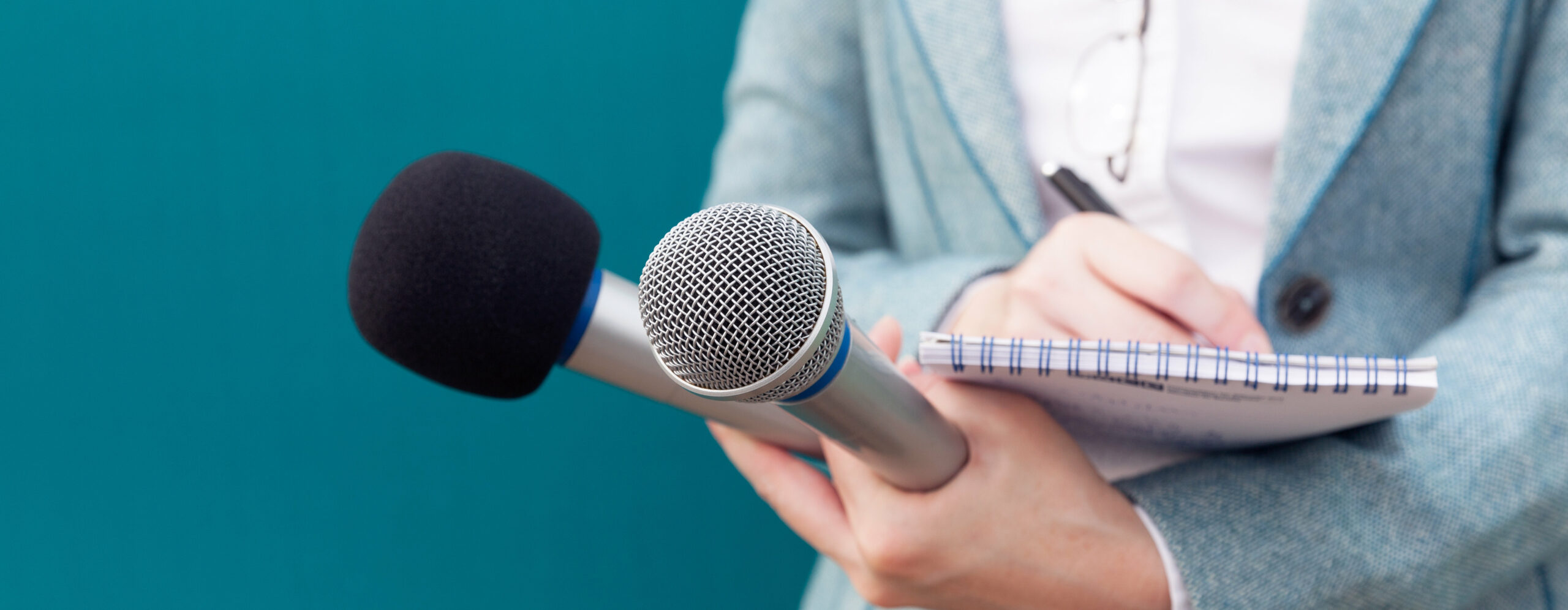 Reporterin mit Notizblock und Mikrofonen in der Hand