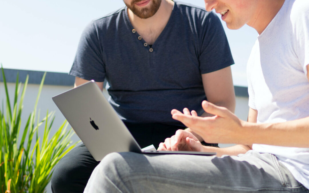 Zwei Männer sitzen mit Laptops auf Terrasse und arbeiten