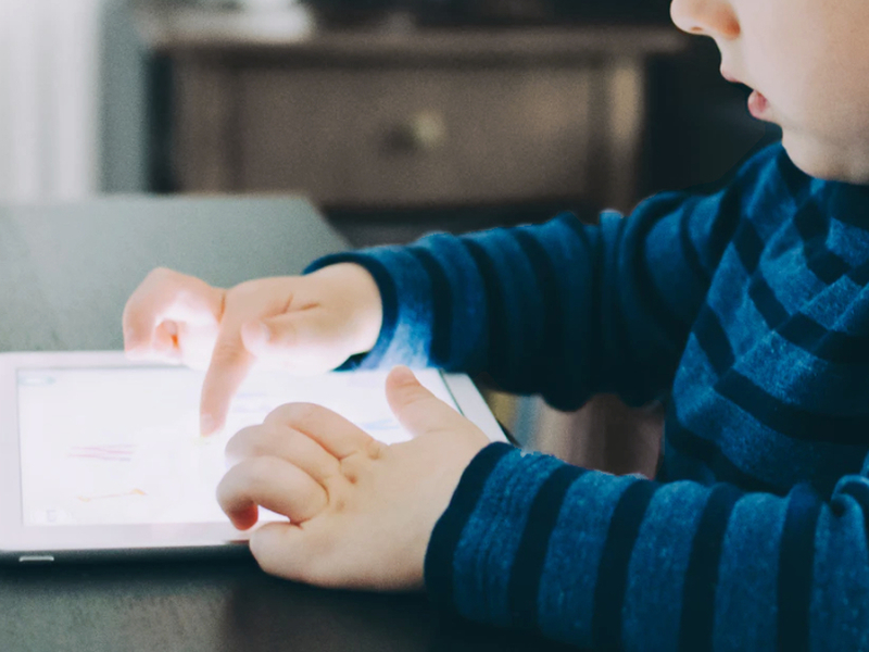 Kind tippt auf beleuchtetem Tablet, das auf dem Tisch liegt