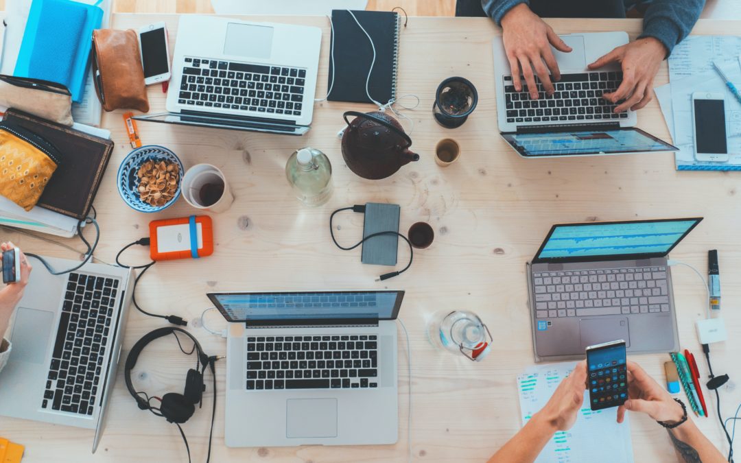 Mitarbeiter sitzen mit Laptops und Handys zusammen an einem Tisch