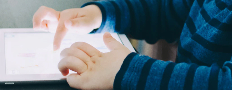 Kind tippt auf beleuchtetem Tablet, das auf dem Tisch liegt