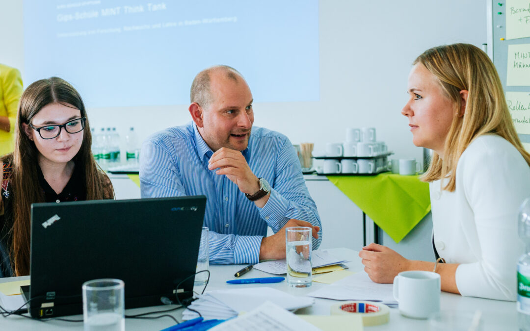 Drei Personen sitzen am Tisch und besprechen sich