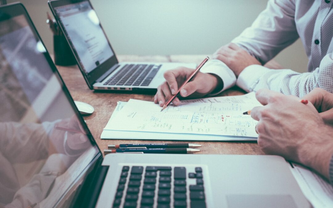 Zwei Männer sitzen am Tisch mit ihren Laptops, Stift und Papier