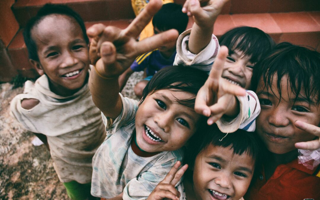 Kinder lachen in die Kamera und machen das Peace-Zeichen