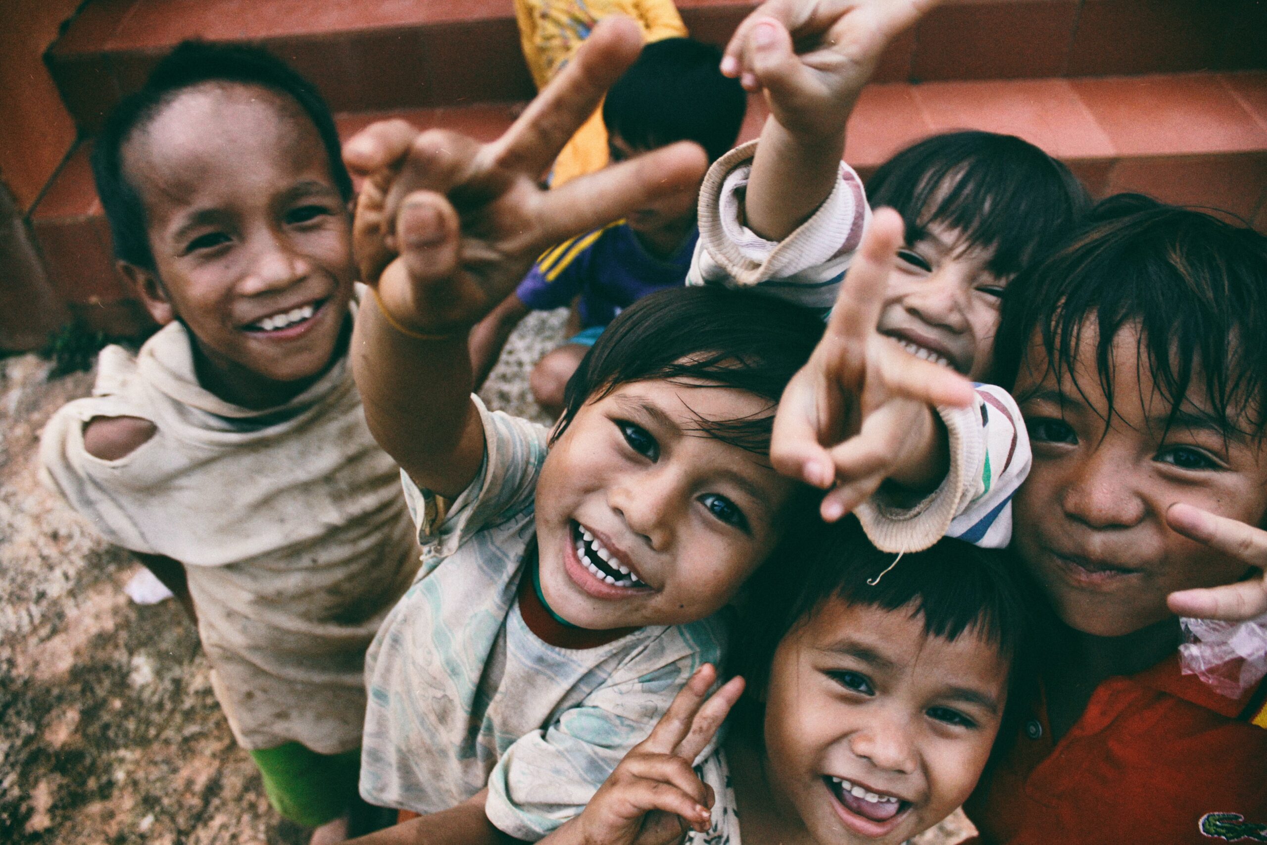 Kinder lachen in die Kamera und machen das Peace-Zeichen