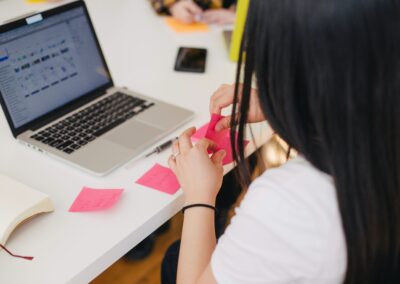 Frau sitzt vor Laptop und macht sich Notizen auf bunte Post-its