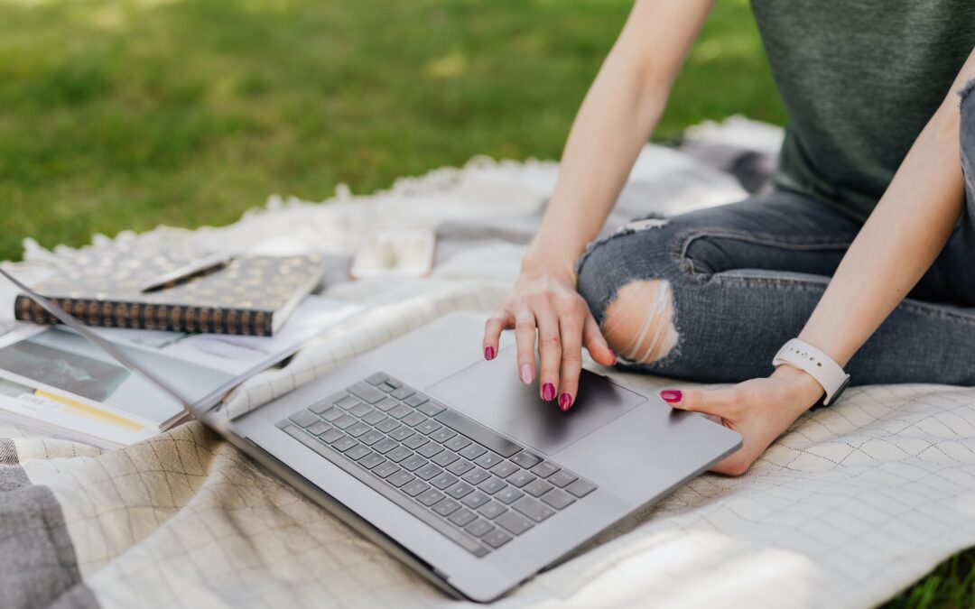 Frau sitzt im Park auf einer Decke mit ihrem Laptop