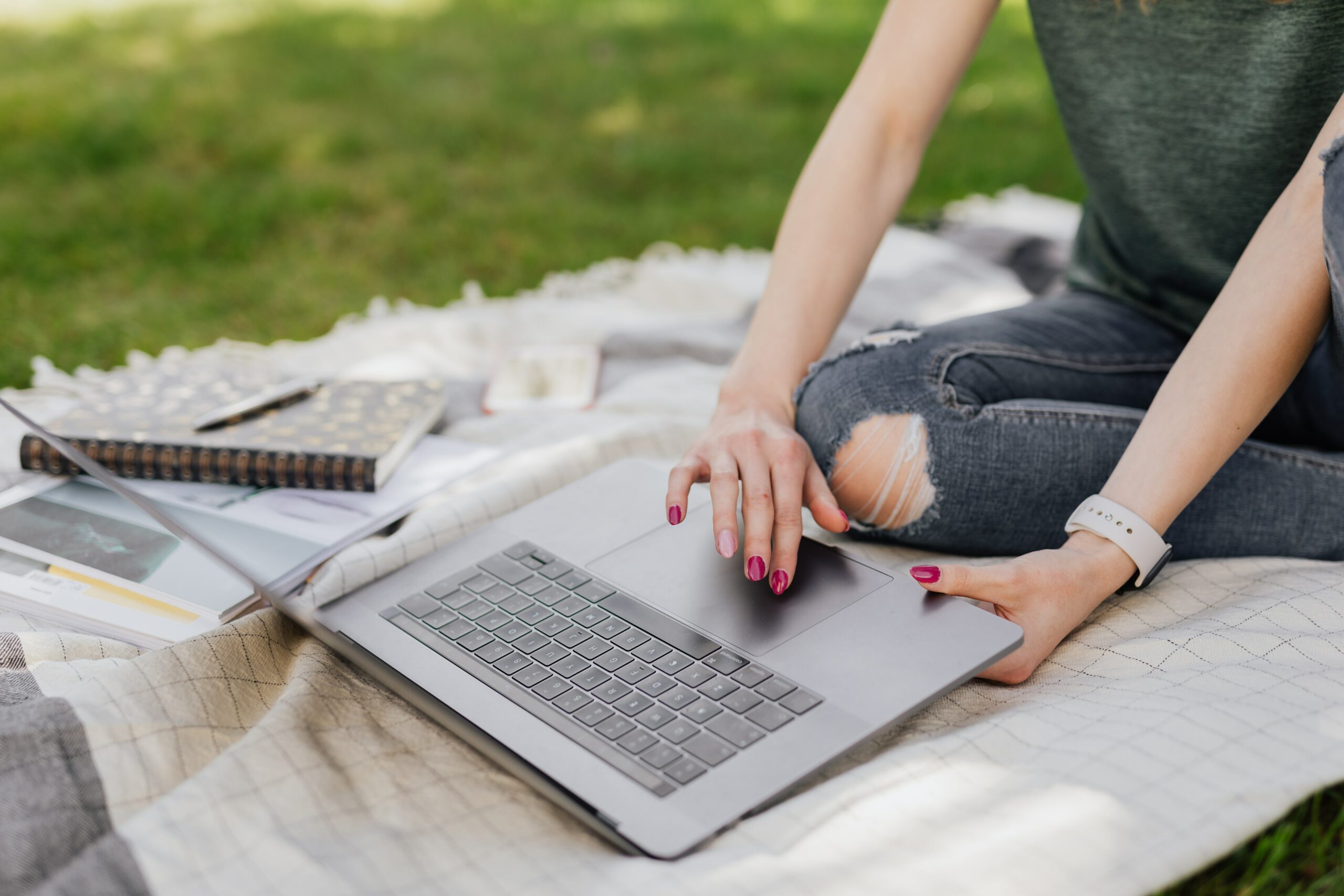 Frau sitzt im Park auf einer Decke mit ihrem Laptop