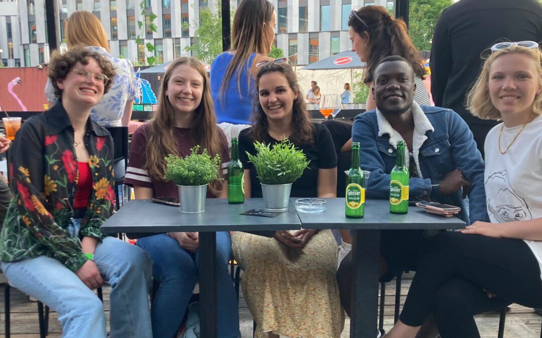 Das Bild zeigt 5 junge Menschen, die auf einer Terrasse an einem Tisch sitzen.